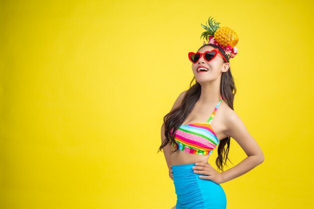 Beautiful woman in a swimsuit holding a pineapple poses on yellow