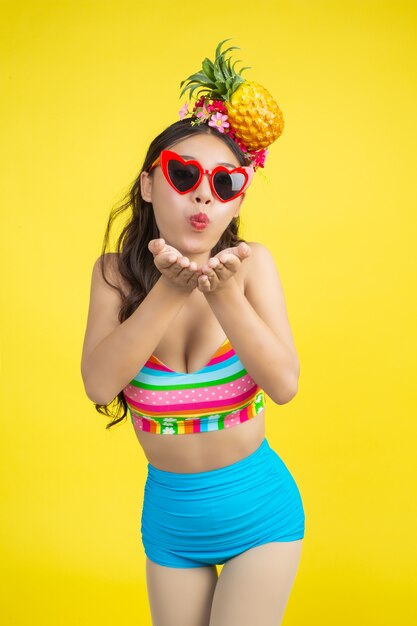 Beautiful woman in a swimsuit holding a pineapple poses on yellow