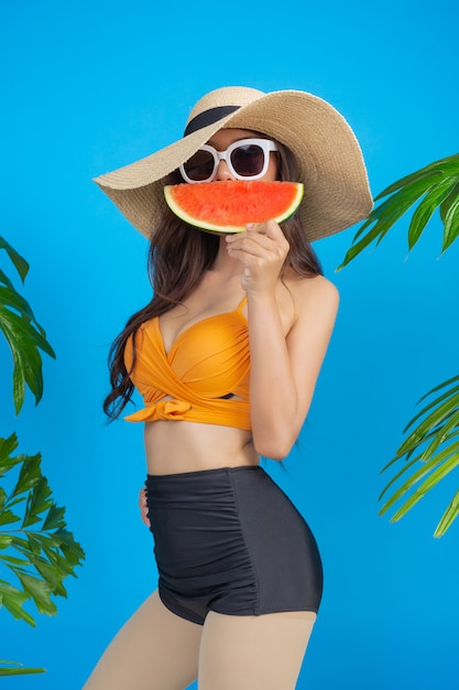 Beautiful woman in a swimsuit holding a watermelon on blue