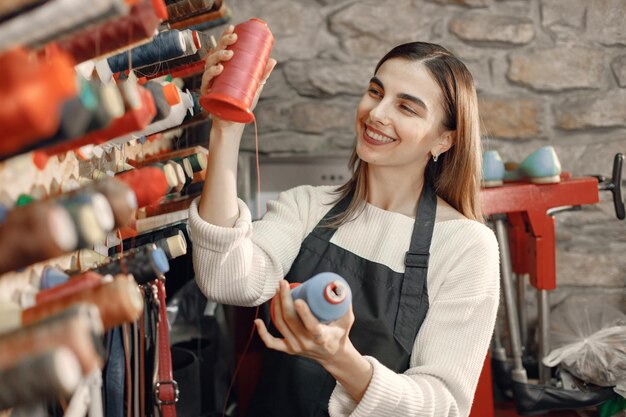 Beautiful woman tailor on background of colored spools of thread for sewing and embroidery Woman wearing an apron Young woman choosing reel of cotton