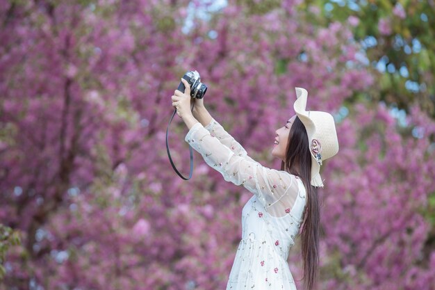 A beautiful woman takes a picture with a film camera in the Sakura flower garden.