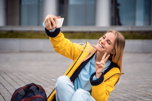 美しい女性がスマートフォンでselfieを取り、スケートボードに座っています。