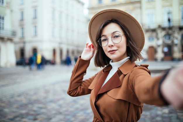 美しい女性が街で彼女の携帯電話を押しながらselfieを取る