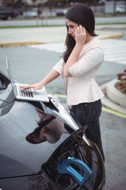 電気自動車を充電しながら携帯電話で話している美しい女性