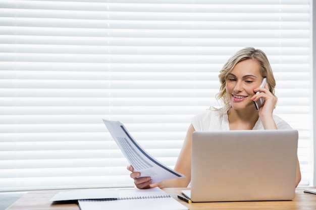 Beautiful woman talking on mobile phone while holding document