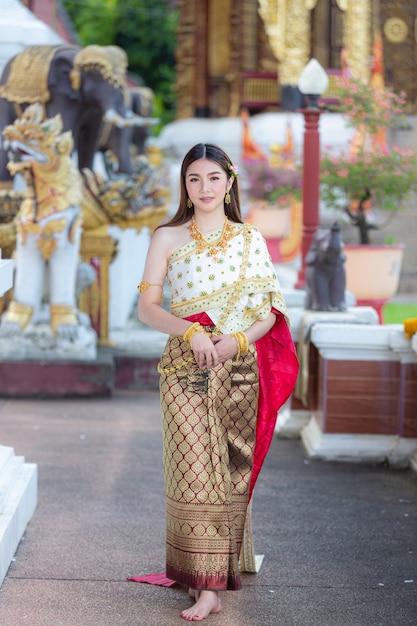 笑顔で寺院に立っているタイの伝統的な衣装の美しい女性