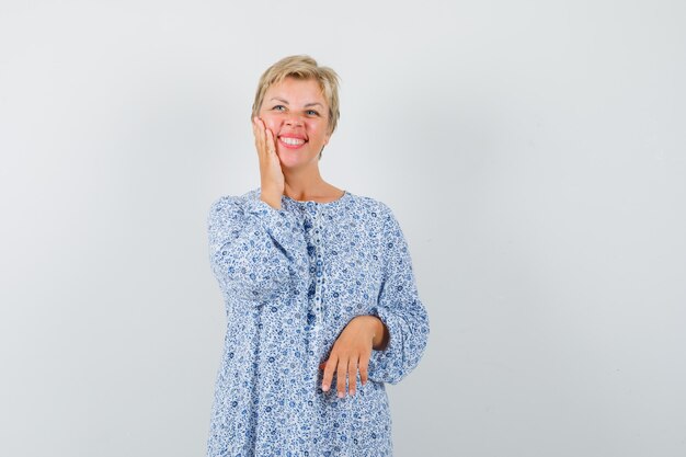 Beautiful woman touching her face in patterned blouse and looking cheery. front view.