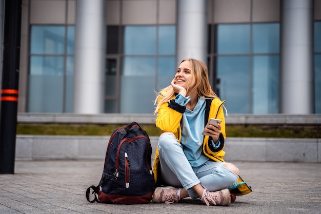 La bella donna usa lo smartphone e si siede sullo skateboard