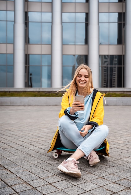 Beautiful woman uses smartphone and sits on skateboard