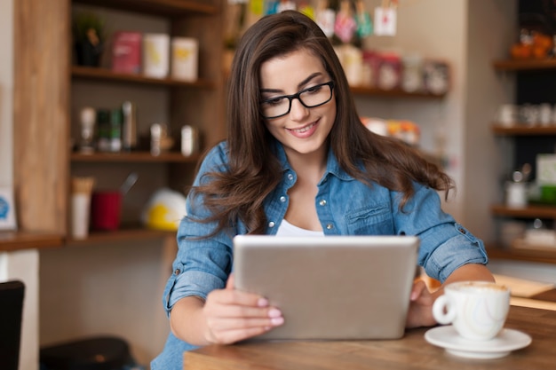 Bella donna che per mezzo della compressa digitale al caffè