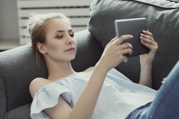 Beautiful woman using digital tablet, lying on sofa