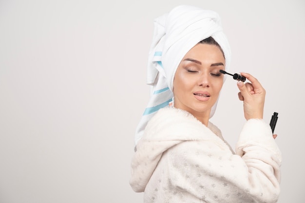 Bella donna che utilizza mascara in asciugamano su uno sfondo bianco.