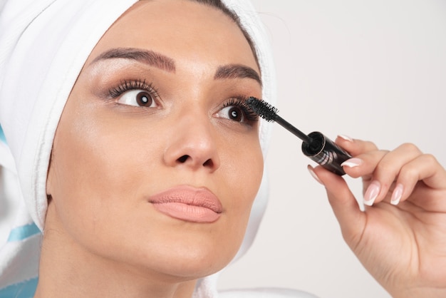 Beautiful woman using mascara in towel on a white space