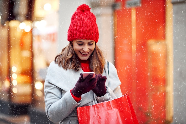 Красивая женщина с помощью мобильного телефона во время покупок в зимнее время