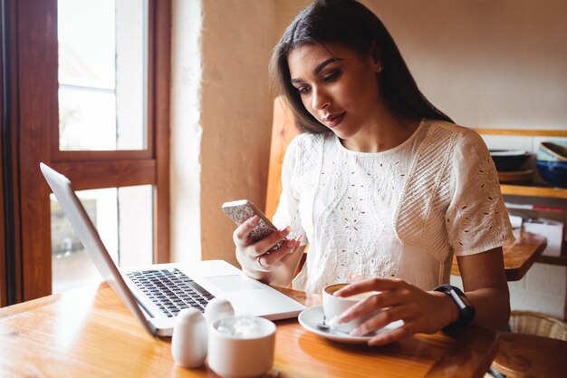 Beautiful woman using mobile phone while having a cup of coffee