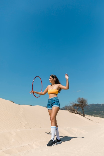 Beautiful woman walking with hula hoop on sand