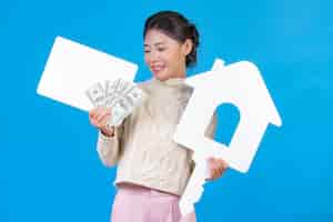 Бесплатное фото Красивая женщина, носить новый с длинными рукавами белый ковер, который держит символ дома. белая доска и долларовая банкнота на сини. торговая