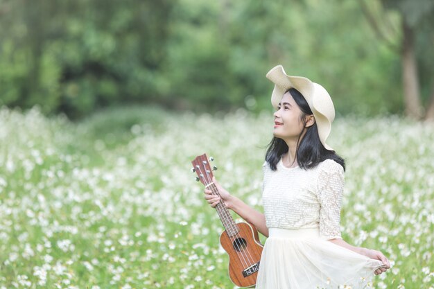 Beautiful woman wearing a cute white dress and holding a ukulele