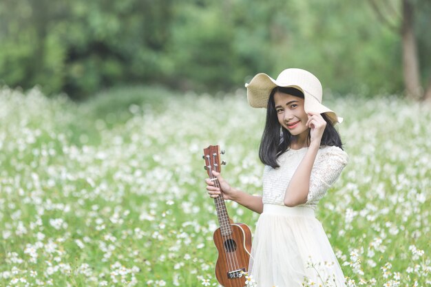 Красивая женщина в милом белом платье и держит гавайскую гитару