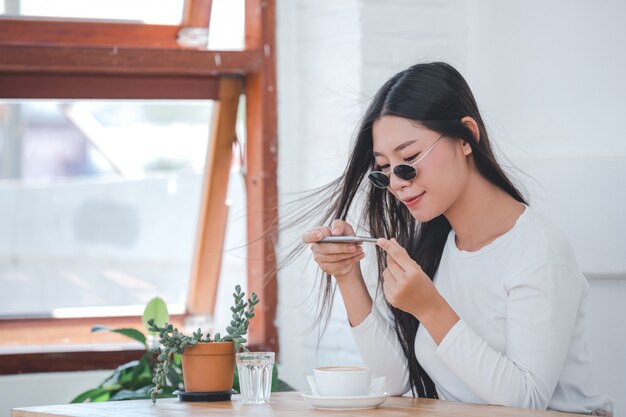 コーヒーショップに座っている長袖の白いシャツを着ている美しい女性