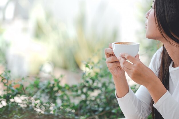 コーヒーショップに座っている長袖の白いシャツを着ている美しい女性