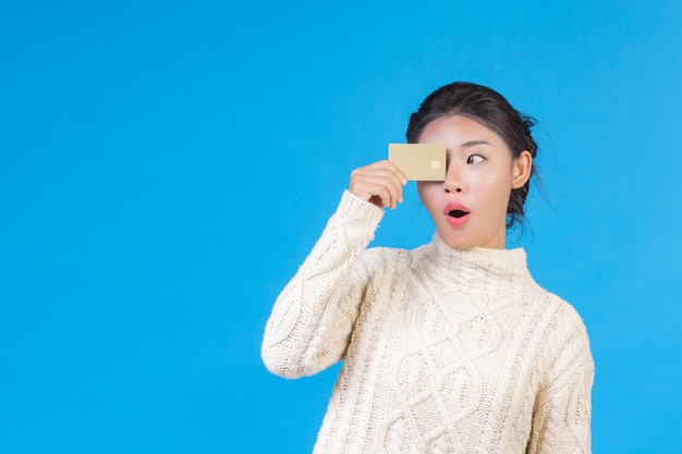 Beautiful woman wearing a new long sleeved white carpet, holding a gold credit card on a blue . Trading .