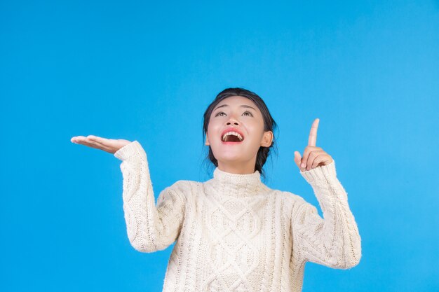 Beautiful woman wearing a new long sleeved white carpet, showing a gesture on a blue . Trading  .