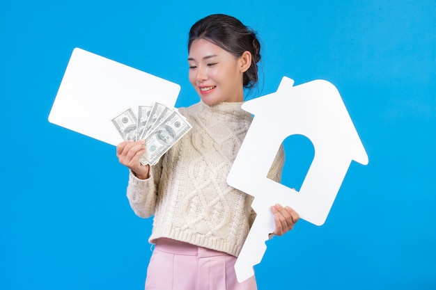 Beautiful woman wearing a new long sleeved white carpet that holds the house symbol. White plaque and dollar bill on a blue . Trading .