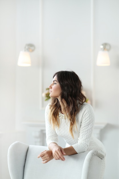 Free photo beautiful woman wearing white dress and sitting in white armchair