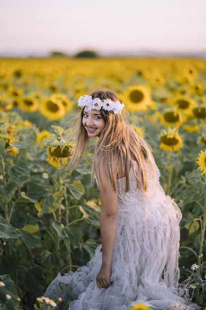 Beautiful woman wearing a white dress, smiling and standing in the sunflower field