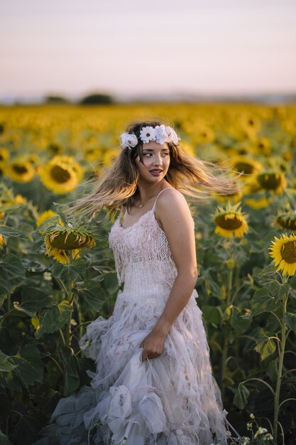 Free photo beautiful woman wearing a white dress and standing in the sunflower field