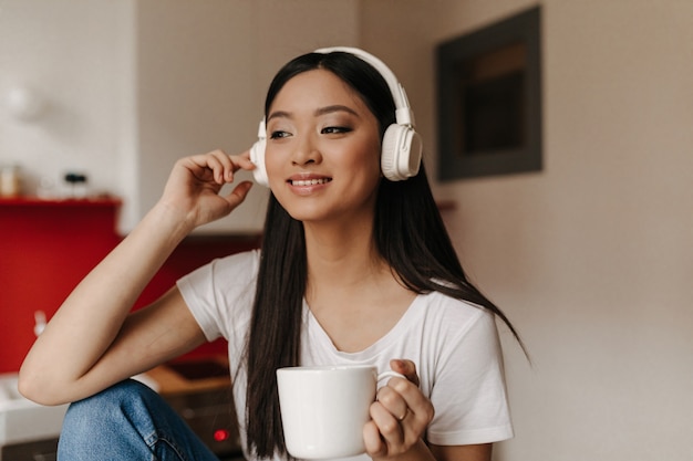 Beautiful woman in white T-shirt and headphones is listening to music over cup of tea