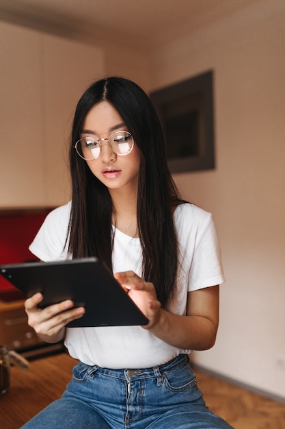 Bella donna in maglietta bianca e occhiali alla moda guarda nello schermo del tablet computer