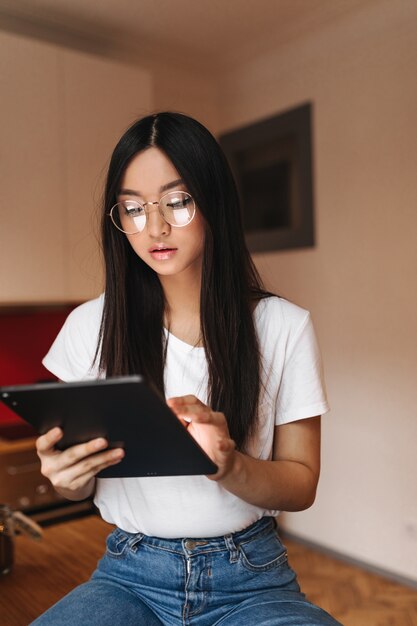 흰색 티셔츠와 세련된 안경에 아름다운 여자가 컴퓨터 태블릿의 화면에 보이는
