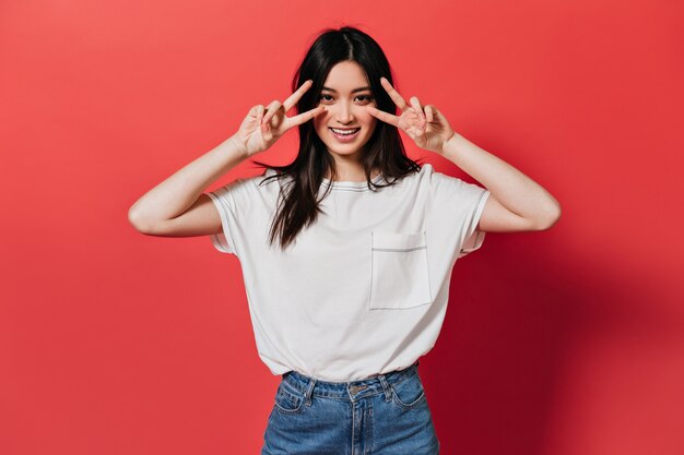 Beautiful woman in white top shows peace sign on isolated wall