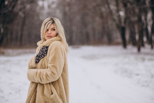 Beautiful woman in winter coat walking in park full of snow