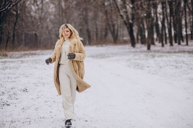 雪の公園を歩く冬のコートを着た美しい女性