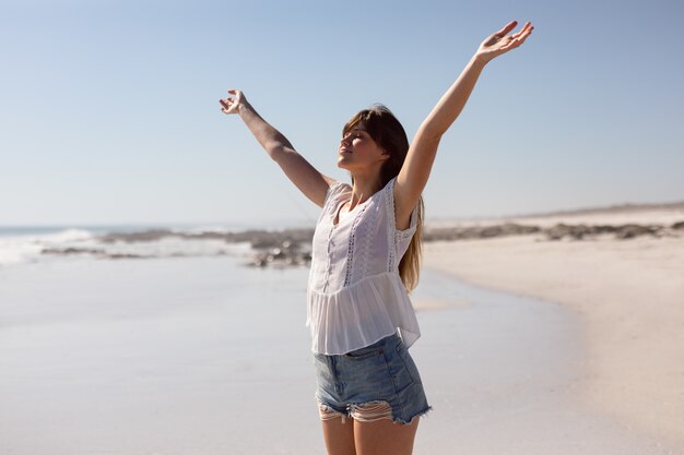 Красивая женщина с вытянутыми руками стоя на пляже в лучах солнца