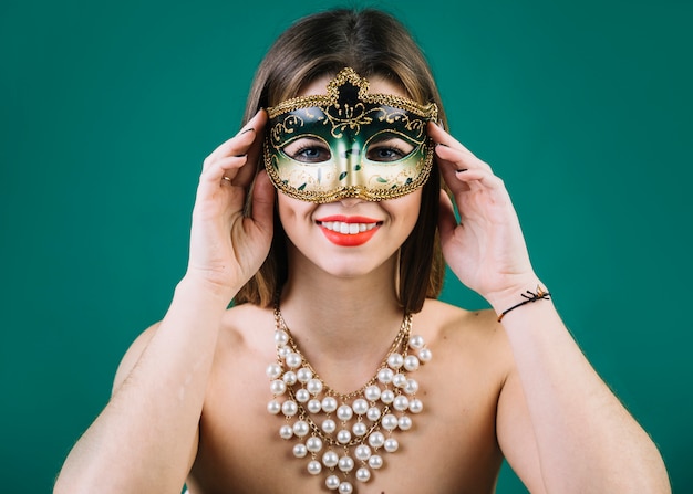 Beautiful woman with beads necklace and carnival mask on green backdrop