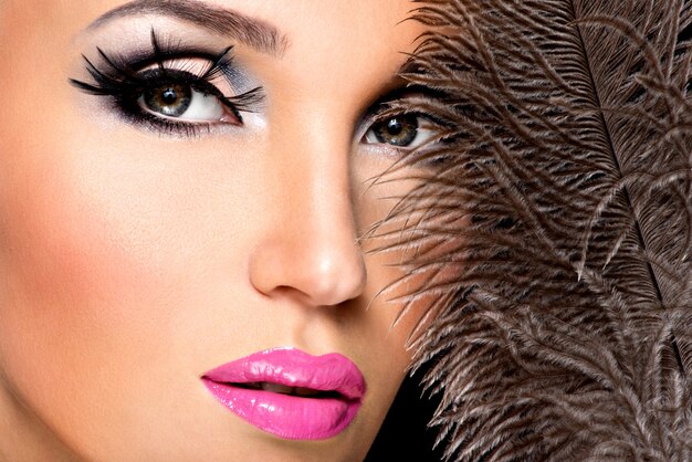 Beautiful woman with bright professional make-up with feathers near the face.
