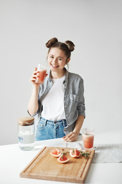 白い壁にグレープフルーツデトックススムージーを飲む笑顔のパンと美しい女性。健康的な食事の栄養