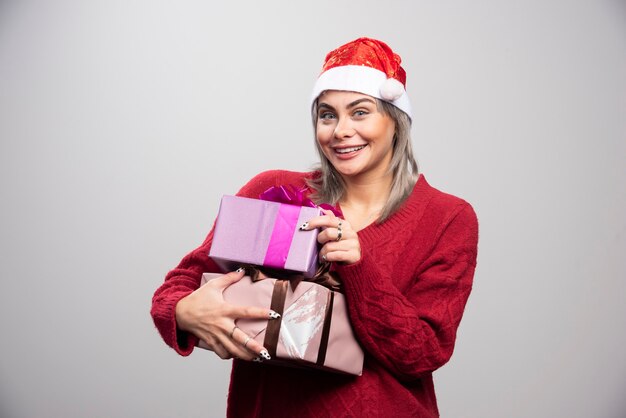 Красивая женщина с рождественскими подарками позирует на сером фоне.