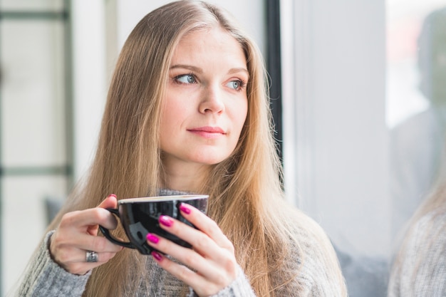 Free photo beautiful woman with coffee looking at window