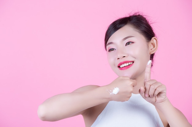 Beautiful woman with cream on the skin on a pink background.