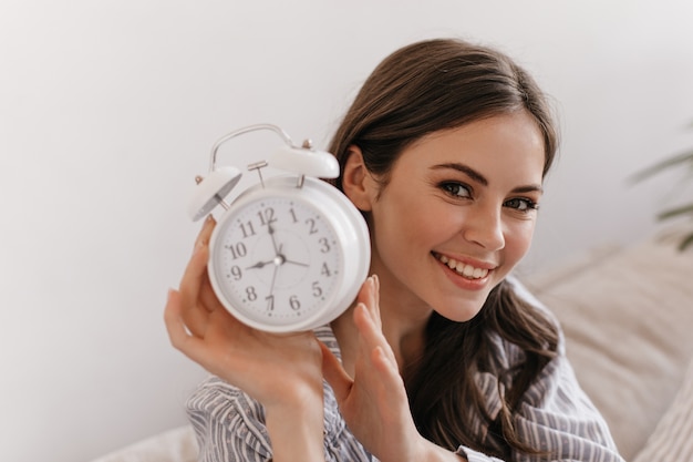 Free photo beautiful woman with dark hair is looking into front and holding large alarm clock