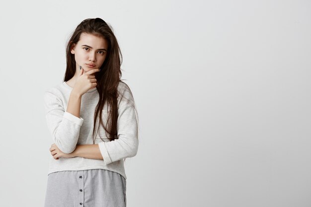 Beautiful woman with dark long hair, dark eyes, keeps hand on chin, looks pensively