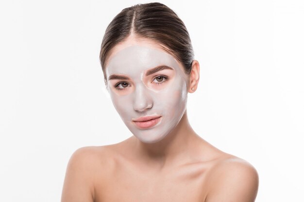 Beautiful woman with eyes closed and white clay facial mask on face on white wall