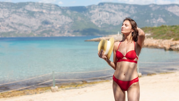 Foto gratuita bella donna con un cappello in piedi sulla spiaggia
