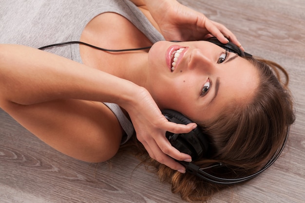 Beautiful woman with headphones lying on the floor