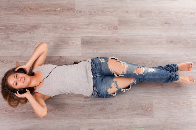 Beautiful woman with headphones lying on the floor